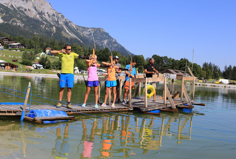 Gruppe am Bogenschießen steht auf einem Steg im Wasser.  | © Erlebnis Rittisberg